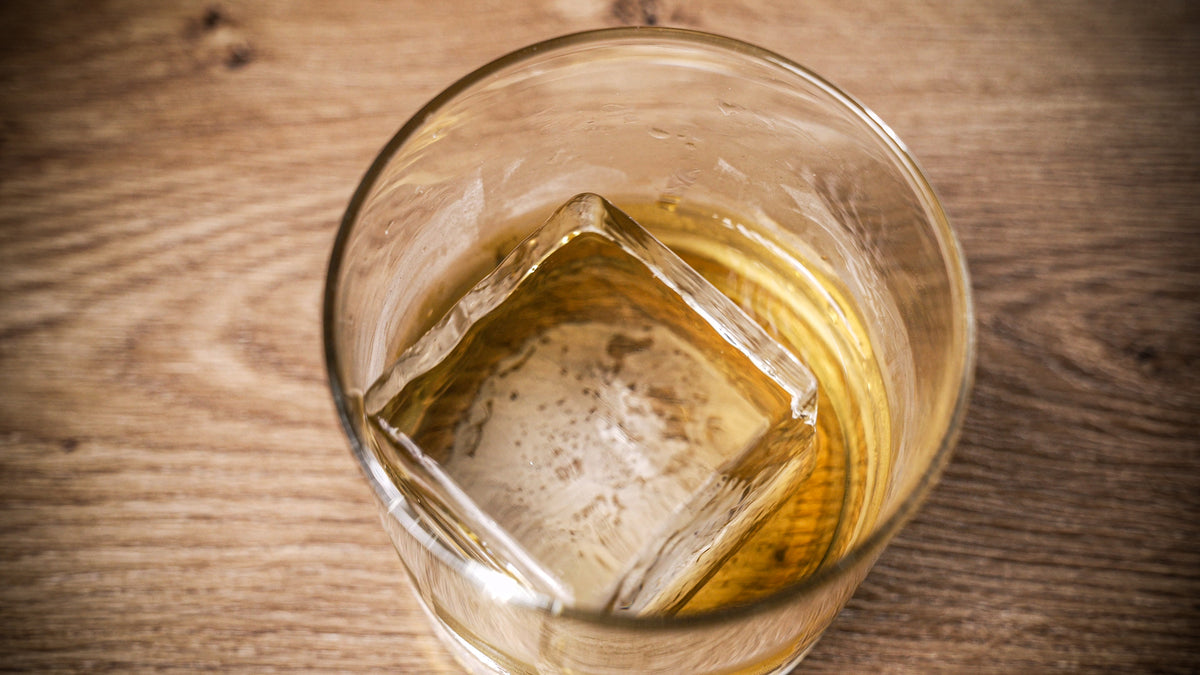 A top-down picture of a highball glass with a clear ice cube in a light brown liquid